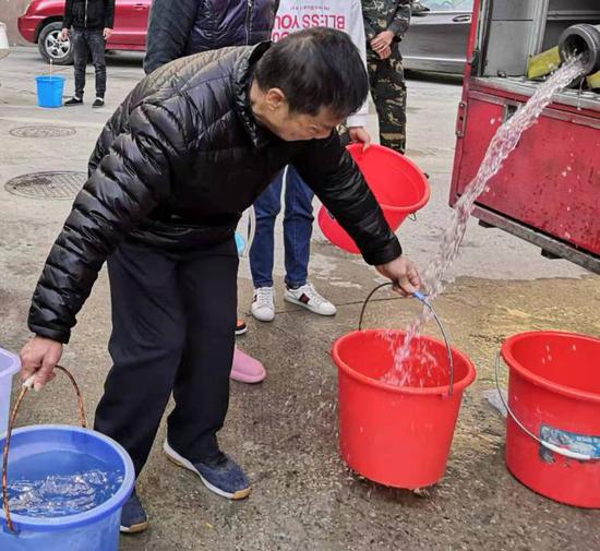 居民在消防车上接水，靠人力一桶一桶提上楼。